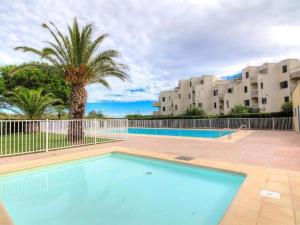 a swimming pool with a palm tree and buildings at Studio cabine, vue mer, piscine in Saint-Cyprien-Plage