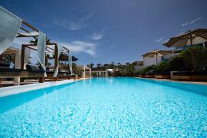 a large blue swimming pool with chairs and umbrellas at Aurora Luxury Suites in Imerovigli