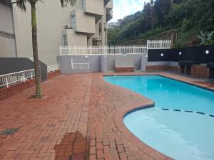 a swimming pool with a brick walkway next to a building at Cozumel 216 in Umdloti