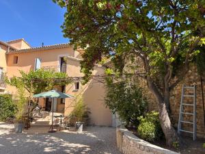 a house with a table and an umbrella and a tree at La Bastide des Dentelles in Roaix
