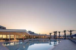 a large swimming pool with palm trees and a building at Rethymno Village in Platanes