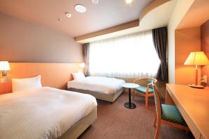 a hotel room with two beds and a table and a window at Hotel Premium Green Hills in Sendai
