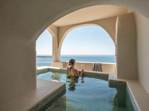 a woman in a swimming pool with the ocean in the background at Art Maisons Oia Castle in Oia
