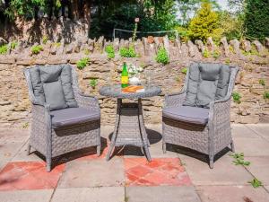 two wicker chairs and a table with a drink at Gardeners Cottage in Putley