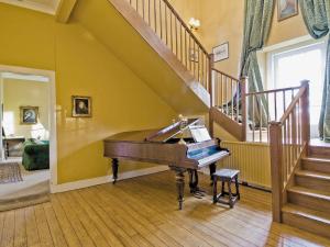 a piano in a living room with a staircase at Lochside Garden House - S4484 in Town Yetholm +14 photos