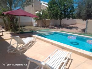 a swimming pool with two chairs and an umbrella at villa Flori Midoun in Djerba