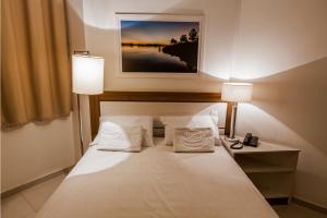 Una cama en una habitación de hotel con dos lámparas. en Hotel Bizzon, en Jequié