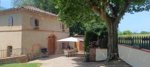 a house with a table and an umbrella and a tree at Le moulin de Christine in Saint-Nauphary