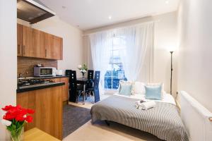 a bedroom with a bed and a kitchen with a window at Elicia's South Kensington Apartment in London