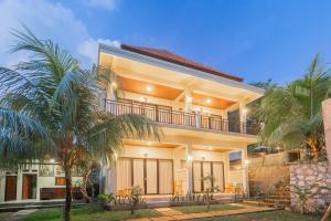 a large house with a balcony and palm trees at Kamasan Nusa Penida By Reccoma in Nusa Penida