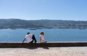 a man and a woman sitting on a wall by the water at Apartamentos turísticos O Estaleiro in Moaña +230 photos