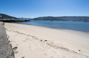 a sandy beach with a pier in the water at Apartamentos turísticos O Estaleiro in Moaña