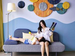 a woman sitting on a couch with a girl reading a book at ibis Styles Vung Tau in Vung Tau