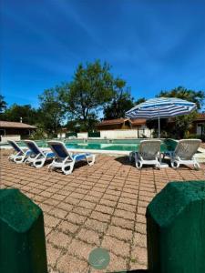 a group of lounge chairs and an umbrella next to a pool at CHALET SUR PILOTIS - 4 personnes - CLIMATISÉ- PISCINE- PROCHE PLAGE in Arès