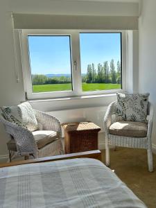 a bedroom with two chairs and a bed and two windows at Sunset View - Luxury accommodation in the Cotswolds in Tewkesbury
