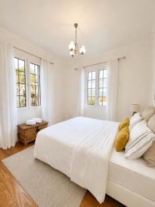 a white bedroom with a large white bed with yellow pillows at A Velha Casa Caboz in Ponta do Sol
