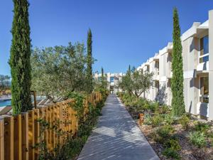 a walkway between buildings with trees and a fence at Novotel Perpignan Nord Rivesaltes in Rivesaltes