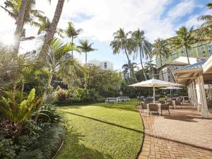 a patio with chairs and an umbrella and palm trees at Novotel Cairns Oasis Resort in Cairns