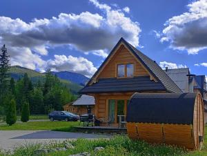 ein Holzhaus mit schwarzem Dach und ein Auto in der Unterkunft DOMEK POLANKA z sauną i widokiem na Tatry in Witów