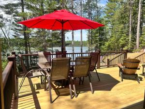 a table and chairs on a deck with a red umbrella at Towering Pines Cottage in Saint Germain