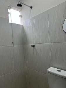 a white tiled bathroom with a toilet and a window at Quarto Selva in Itaquatiara