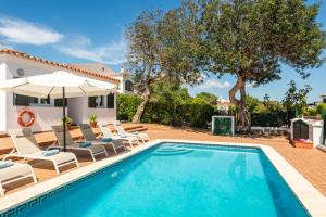 a pool with chairs and an umbrella and a house at Villa Verano in Cala Galdana