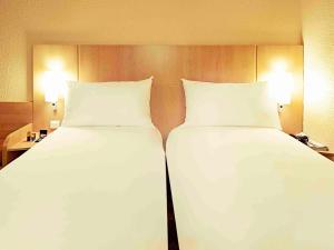 two beds in a hotel room with white sheets and pillows at ibis Abbeville in Abbeville