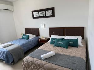 two beds in a hotel room with green pillows at Hotel LHM in Montería