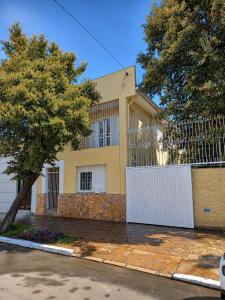 a yellow house with a white fence and a tree at Villa Serena, próx do Aeroporto in Porto Alegre