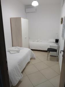 a white bedroom with two beds and a chair at Niko's apartments 1 in Elafonisos