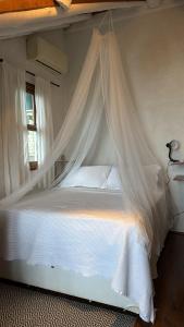 a bedroom with a white bed with a mosquito net at Chalé cercado pela natureza in Imbituba