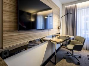 a hotel room with a desk and a tv on a wall at Novotel Den Haag City Centre in The Hague