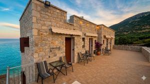 a stone building with chairs on a patio next to the ocean at Ticallisti Rooms by Villa Lagkadaki in Agriliá +33 photos