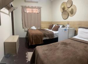 a room with two beds and a refrigerator and a window at Pousada Berro do Bode in Cabaceiras