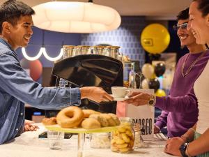 a man handing a plate of doughnuts to a woman at TRIBE Hotel Den Haag Centraal - Opened December 2025 in The Hague
