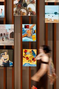 a woman walking past a shelf with pictures on it at Agora, Doha, Autograph Collection in Doha +68 photos