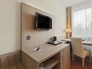 a hotel room with a desk with a tv on the wall at Mercure Hotel Hamburg am Volkspark in Hamburg