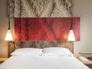 a bedroom with a white bed with two lights above it at Hotel Ibis Coimbra Centro in Coimbra