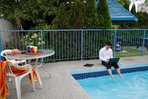 a man sitting on the edge of a pool with a laptop at Recreation Inn and Suites Kelowna in Kelowna