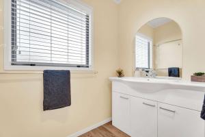 a white bathroom with a sink and a mirror at Fun on the Fairway in Matarangi +20 photos