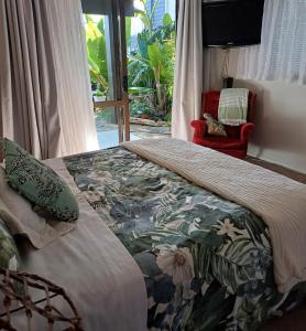 a bedroom with a bed with a floral comforter and a window at Driftwood Sands Studio in Tairua