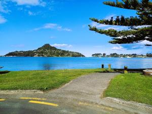 a road next to a body of water with a mountain at Driftwood Sands Studio in Tairua