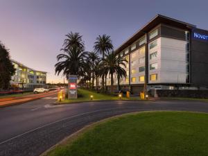 a street in front of a building with palm trees at Novotel Auckland Ellerslie in Auckland