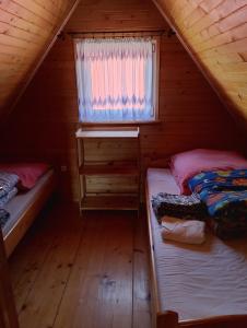 two beds in a wooden cabin with a window at Domek Olchowiec 2 Nad Soliną in Olchowiec