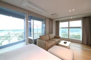 a bedroom with a bed and a couch and windows at Emerson Suites Naksan in Yangyang +16 photos