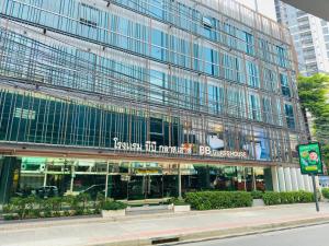 a tall glass building with a sign in front of it at BB Glass House Pattanakrn บีบี กลาสเฮ้าส์ พัฒนาการ in Bangkok