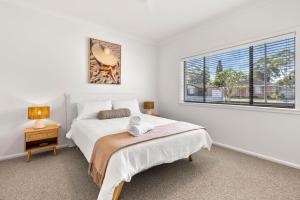 a white bedroom with a bed and a window at Coastline Callala - Fire Pit - Pet Friendly in Callala Beach