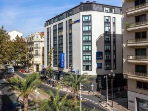 a tall white building on a city street with palm trees at Novotel Suites Cannes Centre in Cannes