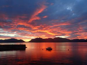 un barco en un cuerpo de agua con una puesta de sol en Loch Linnhe Waterfront Lodges with Hot Tubs, en Glencoe