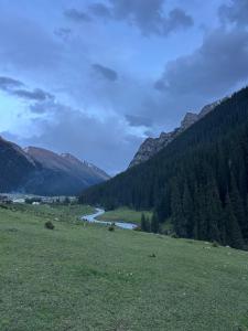 a grassy field with a river and mountains in the background at Alim yurt camp in Mineralʼnyy Istochnik Altyn-Arasan